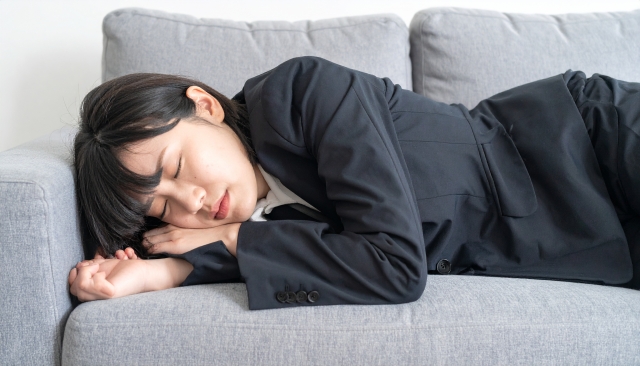 仕事に疲れてソファに横になる女性の様子